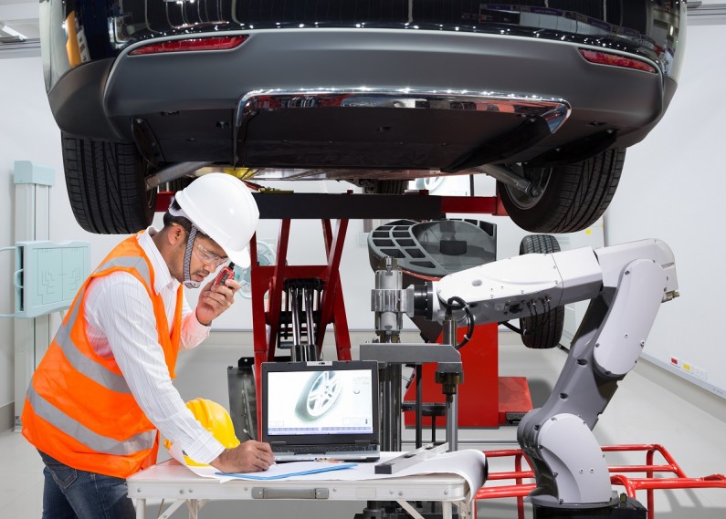 Automotive electrician works on a car alongside a robot