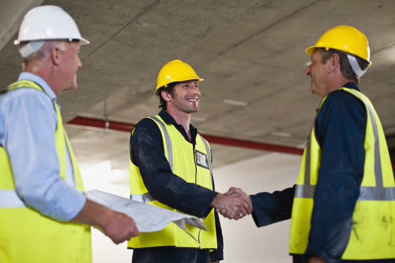 Three men in hard hats greet each other