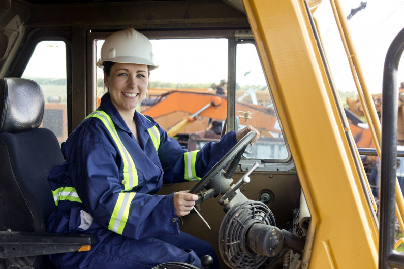 Female construction worker sits in a digger and smiles at the camera.