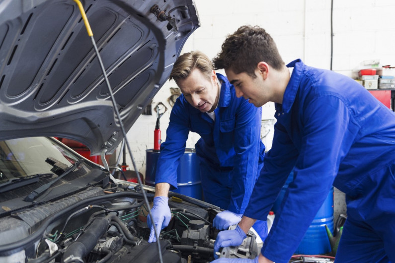 Apprentice and mechanic looking under a car's bonnet
