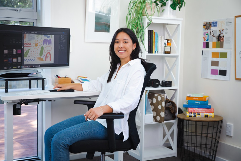 Nicole Sos is facing the camera but sitting at a desk in front of a computer in an office 