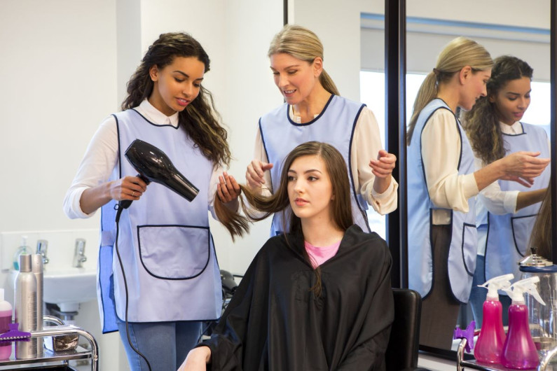 Hairdressing students watch a woman blow dry a person's hari