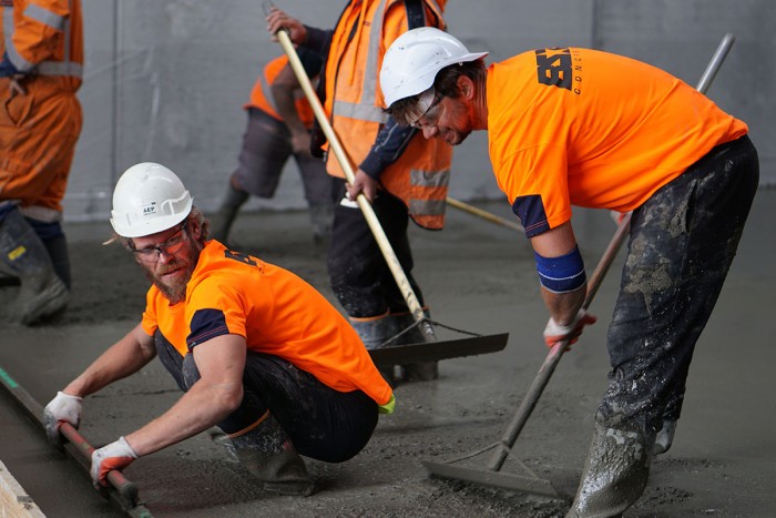 Two workers in high-visibility clothing lay concrete at a construction site