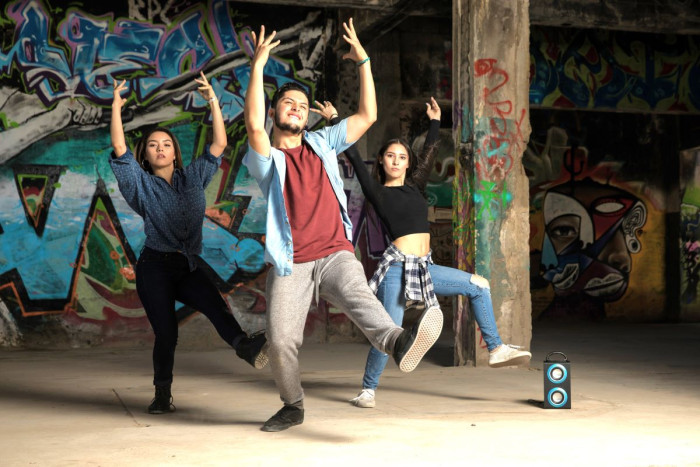 Three people in casual dress dance in front of graffiti