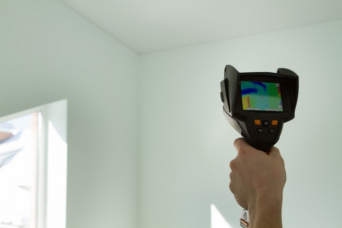 An energy auditor holds up a thermal imaging device to check heat loss in a room