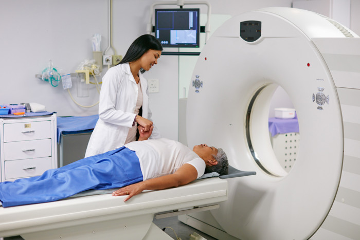 A female medical imaging technologist standing next to a patient on a scanning machine