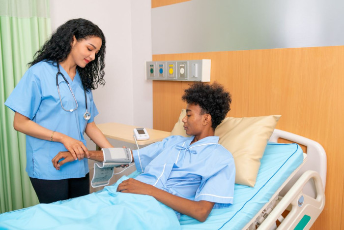 A nurse in uniform wraps a blood pressure cuff around the arm of a boy in a hospital bed
