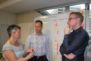 Two people standing next to a whiteboard listen to a scrum master give feedback