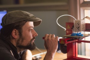 A man observes a 3D printer printing a plastic object.