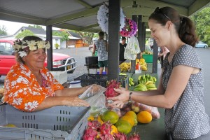 A woman at a market holds open a plastic bag while another puts in some dragon fruit.